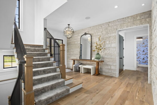 A foyer with a decorative pendant light, stone feature wall, and a switchback staircase with a runner carpet.
