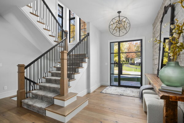 A foyer with a glass front door and sidelight, a decorative pendant light, and a switchback staircase with a runner carpet.