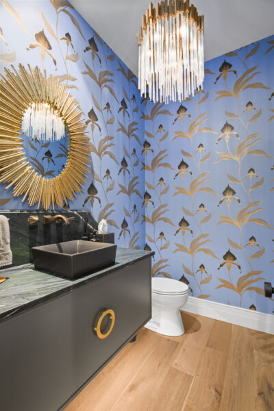 A bathroom with graphic floral motif wallpaper, a statement pendant light, an Art Deco sunburst mirror, and a single vanity with a vessel sink.