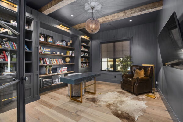 A home office space with charcoal and natural wood finishes, a feature wall of built-in shelving, and a leather club chair.