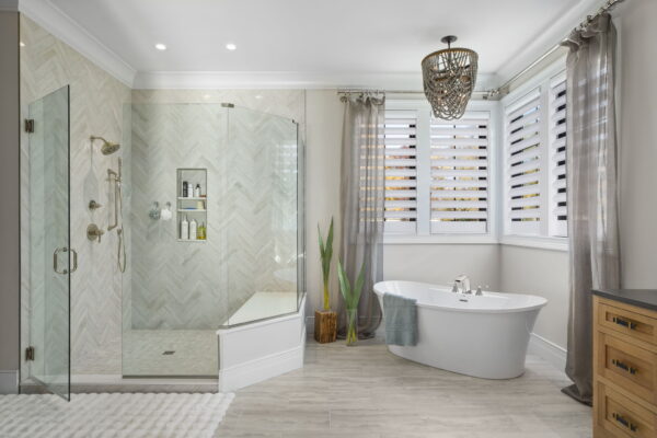 A bathroom with a glass surround walk-in shower, a soaking tub, light gray tile flooring, and a plush rug.