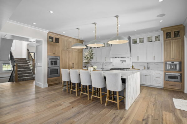 A kitchen with floor-to-ceiling cabinets in white and natural wood, white marble countertops and backsplash, a large island with seating, and wood flooring.