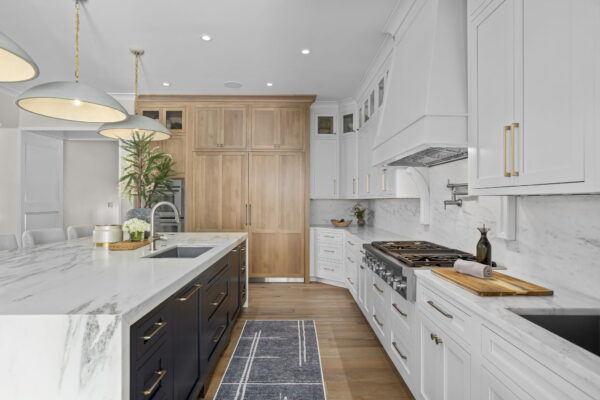 A kitchen with floor-to-ceiling cabinets in white and natural wood, white marble countertops and backsplash, a large island with a sink, and wood flooring.
