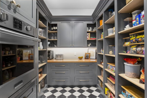 A walk-in pantry with gray cabinets, oak shelving, and a checkerboard floor in a diagonal layout.