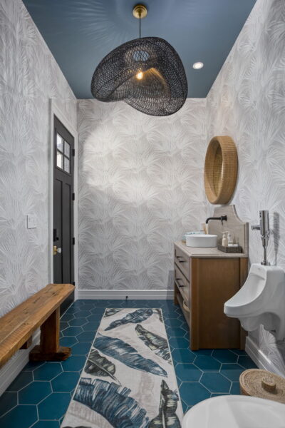 A bathroom with a blue ceiling, tropical leaf motif wallpaper, blue hexagonal floor tile, and an organically shaped wire mesh pendant light.