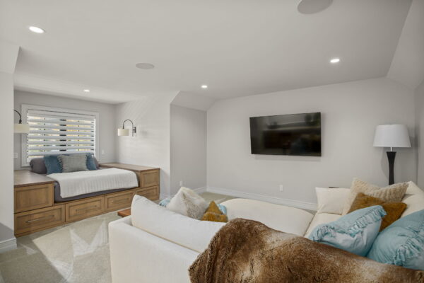 A platform window seat with storage and a sectional in front of a wall-mounted TV in a carpeted room.