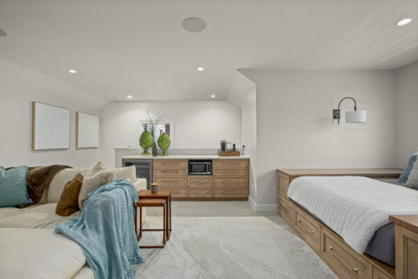 A carpeted studio space with a kitchenette, a sectional, and a platform bed with storage.