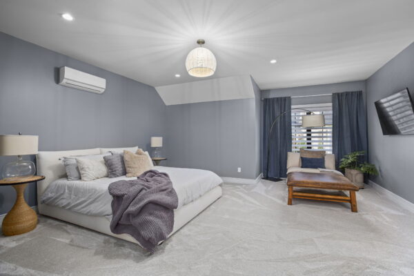 A large bed with an upholstered frame and a lounge chair in front of a window in a carpeted room.