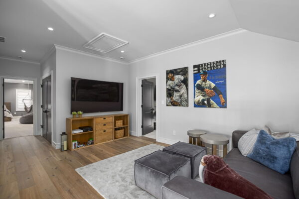 A gray upholstered sofa with two matching ottomans in front of a wall-mounted TV in a transitional space with medium wood flooring.