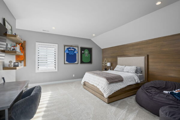 A wooden bed and large bean bags set against a wood-paneled wall in a carpeted room with sports decor.