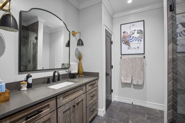 A single vanity with dark wood cabinets, a dark stone countertop, dark fixtures, and bell sconces flanking an arched mirror.