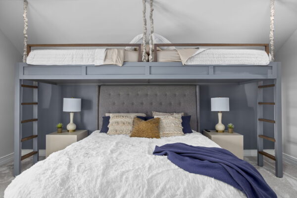A queen size bed flanked by ladders that lead up to two lofted beds with wooden safety railings.
