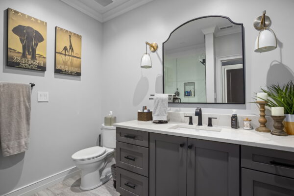 A single vanity with dark gray cabinets, a white stone countertop, dark fixtures, and bell sconces flanking an arched mirror.
