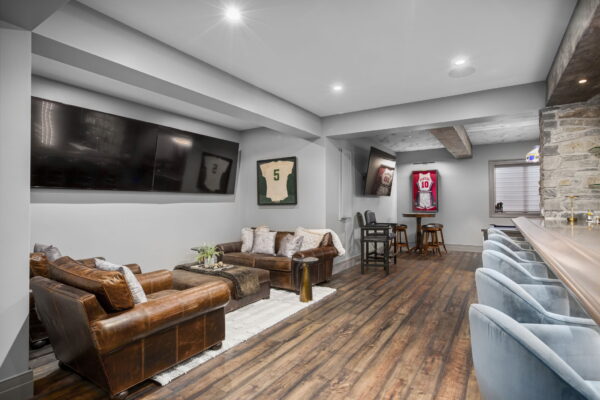 A leather sofa and two matching armchairs face each other next to a wall with two mounted TVs.