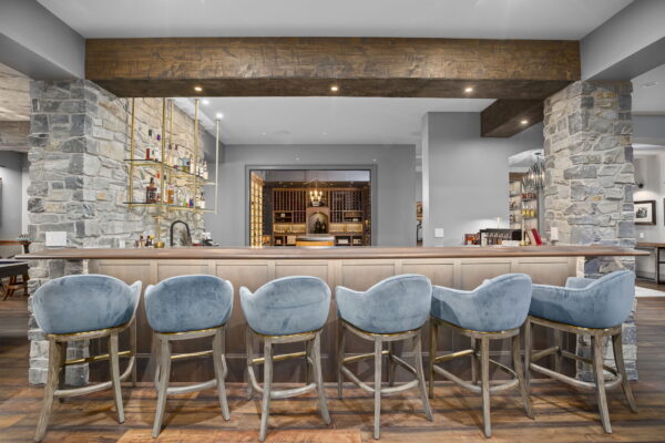 Six bar-height stools upholstered in light blue suede in front of a bar with wood finishes.