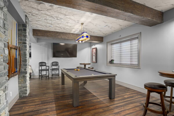 A pool table in the center of a room with rustic wood flooring.
