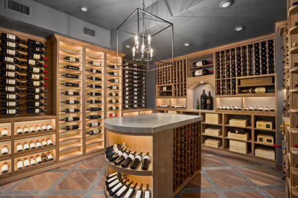 A spacious wine cellar with built-in open storage around the perimeter, a central island, and charcoal and wood finishes.