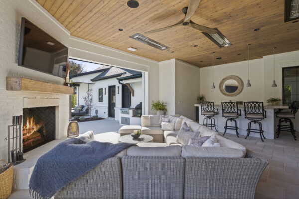 An outdoor lounge space with a wicker sectional, a fireplace, and a wall-mounted TV.