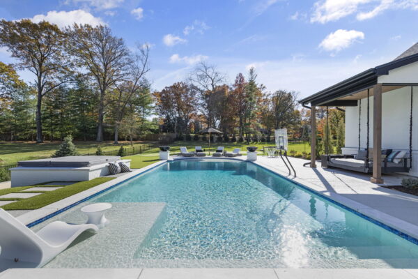 An in-ground pool with a Baja shelf, basketball hoop, and lounge seating.