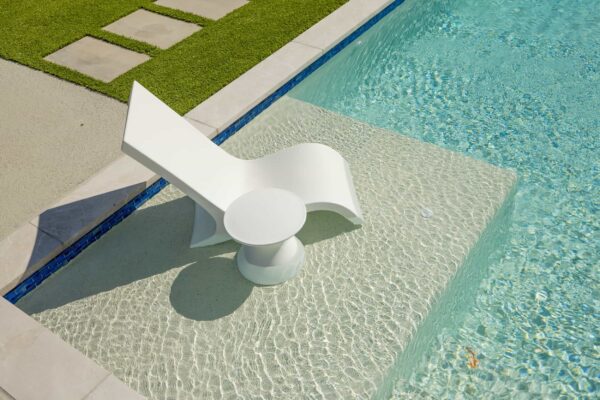 An outdoor lounge chair and matching side table sit on a Baja shelf in a pool.