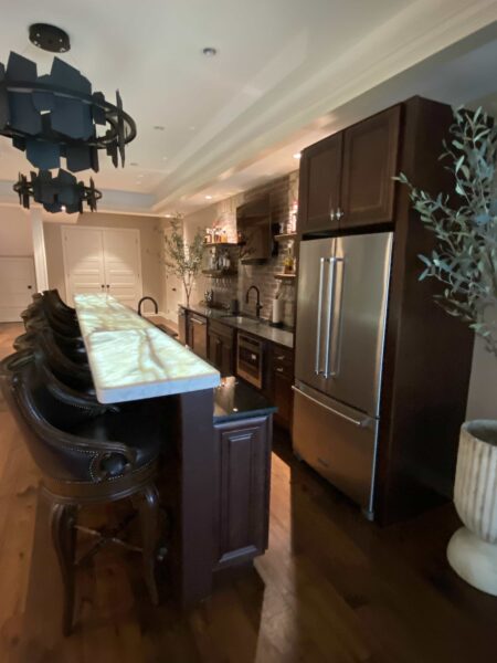 A bar area with dark wood and brick finishes, a stainless steel French door refrigerator, and a polished white stone countertop.