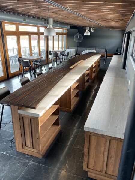 A bar that has a wood base with built-in shelving and a contrasting tiered countertop.