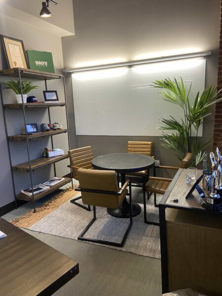 Four leather and steel chairs around a black circular table in a room with exposed brick walls and a dry erase board.