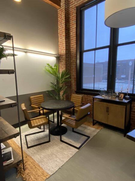 Four leather and steel chairs around a black circular table in a room with exposed brick walls.