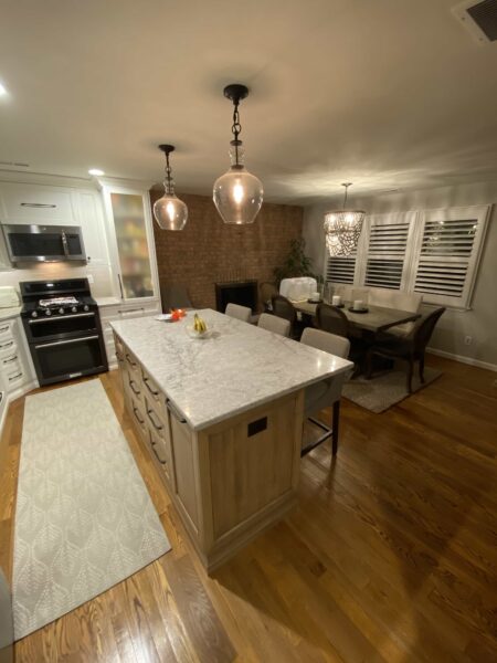 A kitchen with white and natural wood cabinets, white stone countertops, an island with seating, and a dining table with chairs.