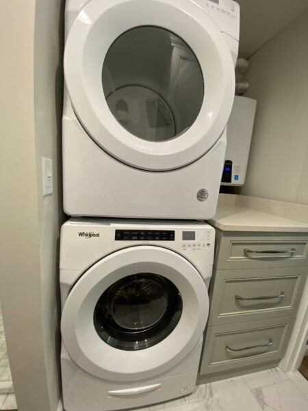 A stacked front load washer and dryer next to a set of drawers with a work surface.