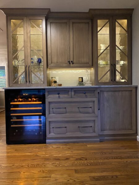 A dry bar area with neutral wood finishes, glass front cabinet doors, and a wine cooler.