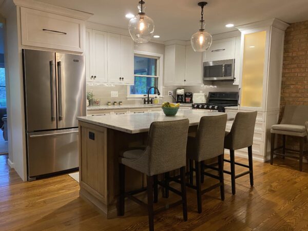 A kitchen with white cabinets, white stone countertops, a stainless steel French door refrigerator, and an island with seating.