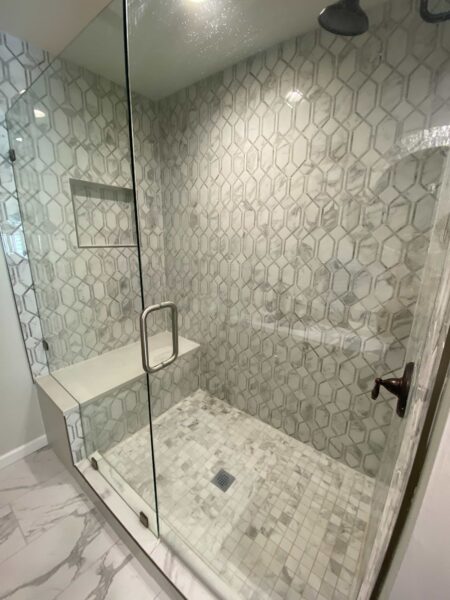 A shower with glass doors, marble mosaic tile, and a built-in bench.
