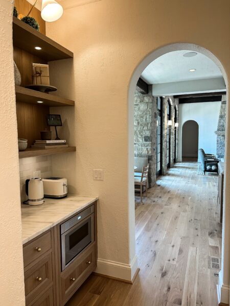 An arched doorway frames a view of the living area from inside a butler's pantry.