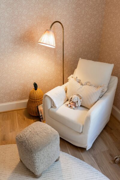 An arched brass floor lamp next to a white upholstered armchair and an ottoman upholstered in a neutral shearling.