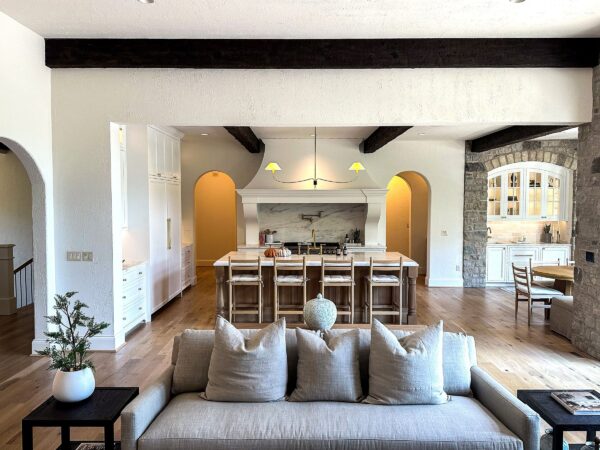 Three chopped pillows on a sofa upholstered in neutral fabric and a view of a kitchen island and custom range hood in the background.