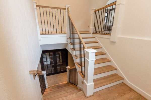 A staircase with white risers and newel posts, white oak treads and handrails, and dark metal balusters.