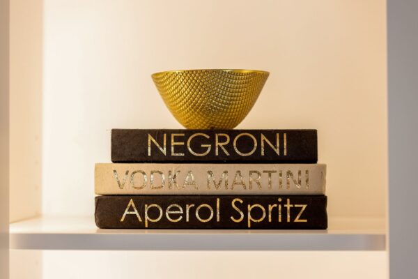 A gold bowl on top of a stack of books titled "Negroni", "Vodka Martini", and "Aperol Spritz".