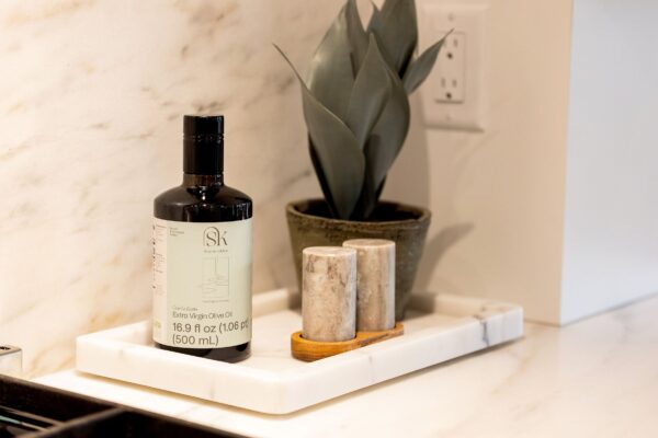 A bottle of Shayna's Kitchen extra virgin olive oil next to a pair of stone salt and pepper shakers and a potted plant.