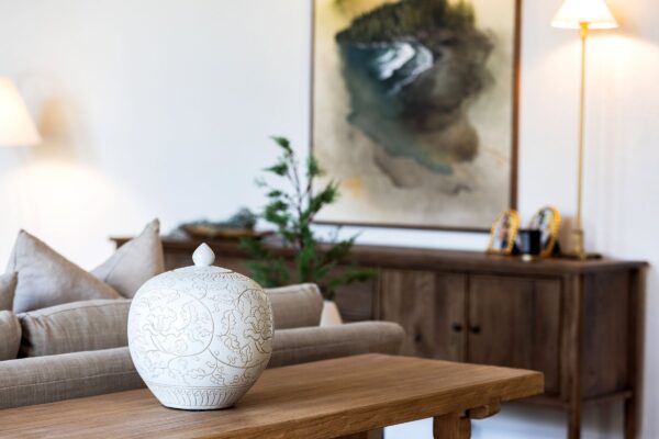 A ceramic vessel engraved with a floral pattern that sits on top of a wood sofa table.