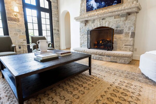 A two-tiered dark wood coffee table set on a low-pile rug in front of a gray stone fireplace.