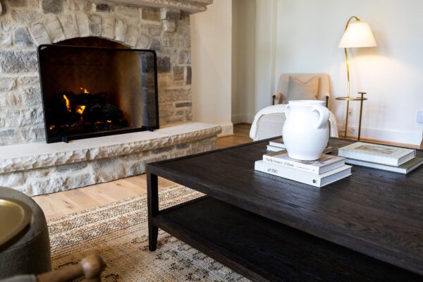 A low, dark wood coffee table set on a low-pile rug in front of a gray stone fireplace.