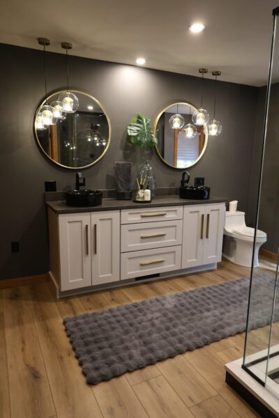 Bathroom with matte charcoal‑gray walls, oak plank floors, white shaker vanity with black vessel sinks, black hardware, round mirrors, and glass globe pendants.