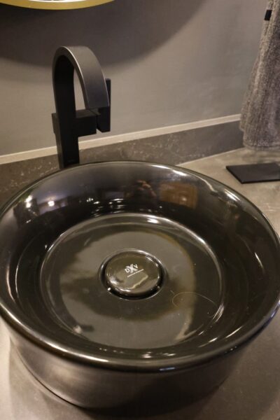 Matte black faucet above a black vessel sink on dark stone countertop.