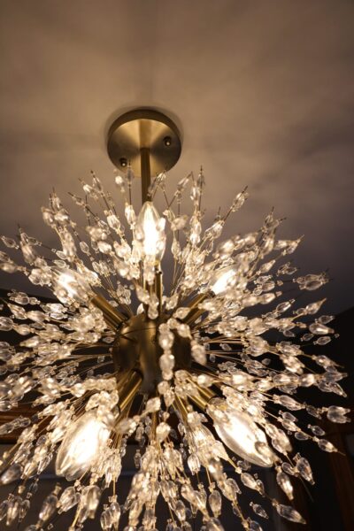 Brass sputnik-style chandelier with radiating polished brass rods and faceted clear glass crystal droplets, casting warm ambient light.