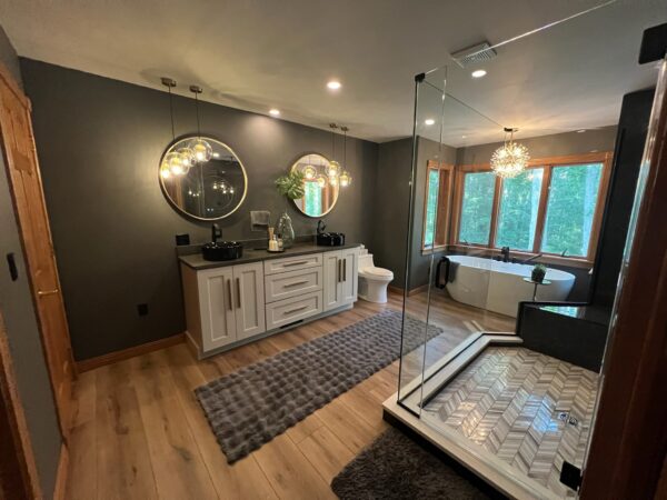 Bathroom with charcoal walls, freestanding tub, glass shower with herringbone tile and black vessel sinks on a double shaker vanity.