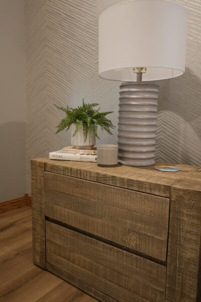 Reclaimed oak sideboard displaying a ceramic table lamp with drum shade and a potted fern against a wall with a neutral-colored chevron pattern.