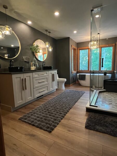 Bathroom with charcoal walls, freestanding tub, glass shower with herringbone tile and black vessel sinks on a double shaker vanity.