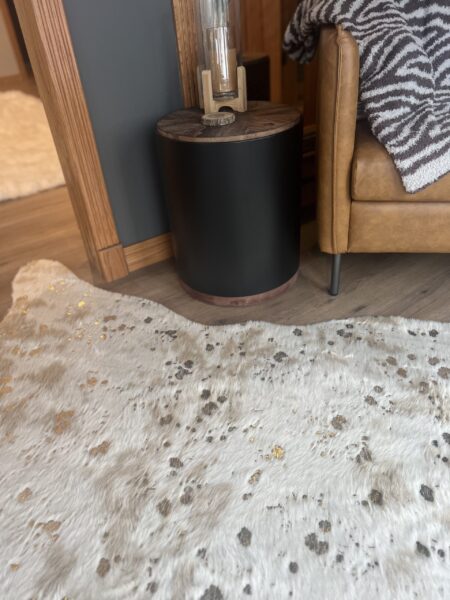 White cowhide rug with gold foil flecks under a tan leather sofa with zebra-print throw.