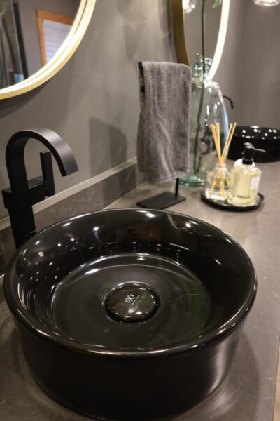 Vanity with black vessel sink and matte black faucet over dark stone countertop.